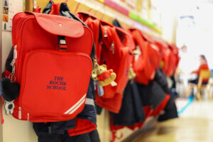 Row of bright red backpacks hanging on a store shelf, with school logo visible on the front pockets