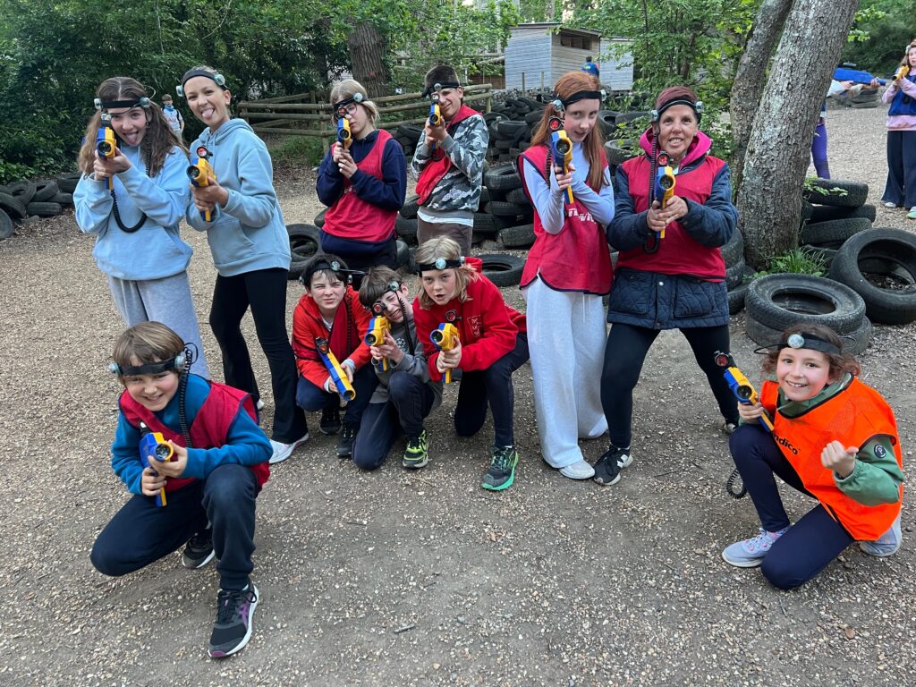 Group of kids with headlamps posing outdoors, holding yellow toy blasters, tires stacked in the background.