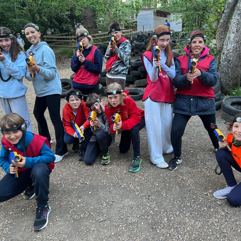 Group of kids with headlamps posing outdoors, holding yellow toy blasters, tires stacked in the background.